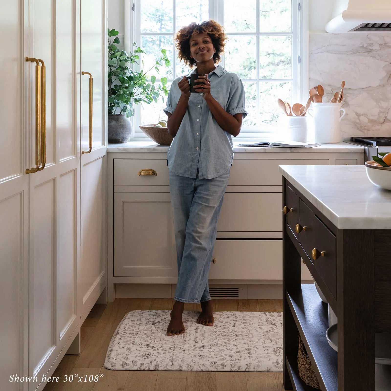 Emile latte neutral floral boho kitchen mat shown in kitchen with woman drinking coffee standing on size 30x108