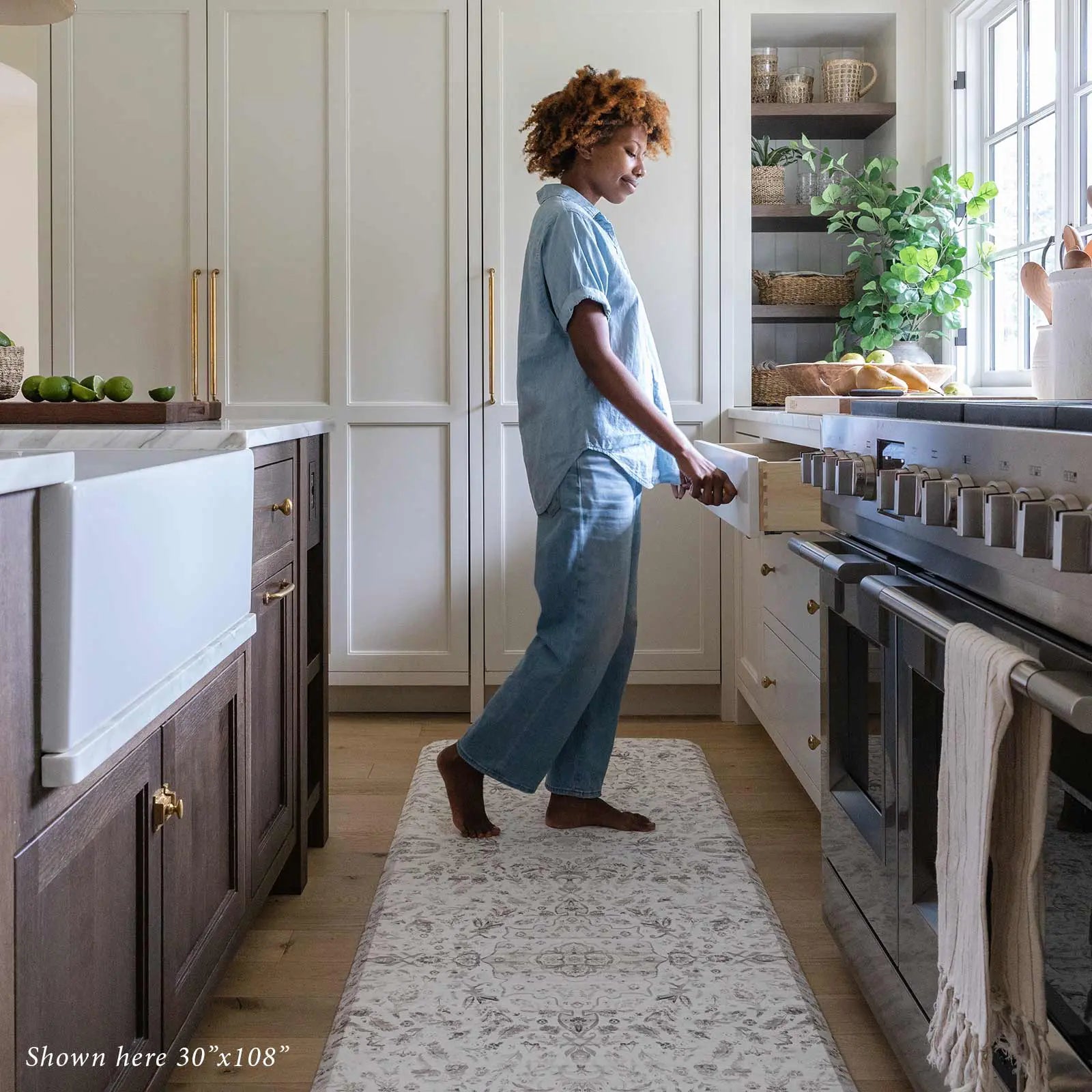 Emile latte beige and gray floral boho kitchen mat shown in kitchen with woman opening a drawer standing on size 30x108