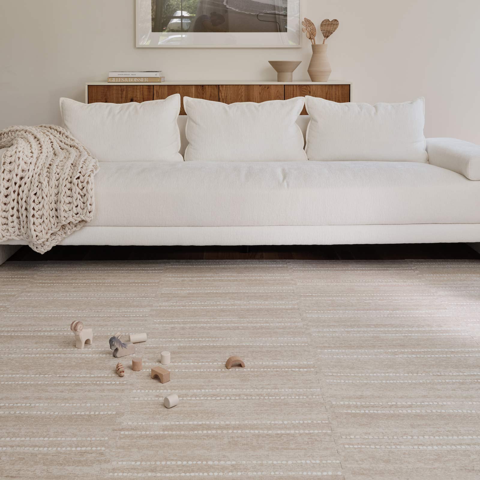 Aspen toast neutral minimal stripe little nomad play mat shown in a living room under a white sofa with chunky knit blanket. Wooden blocks laid out on the mat in front of the sofa.