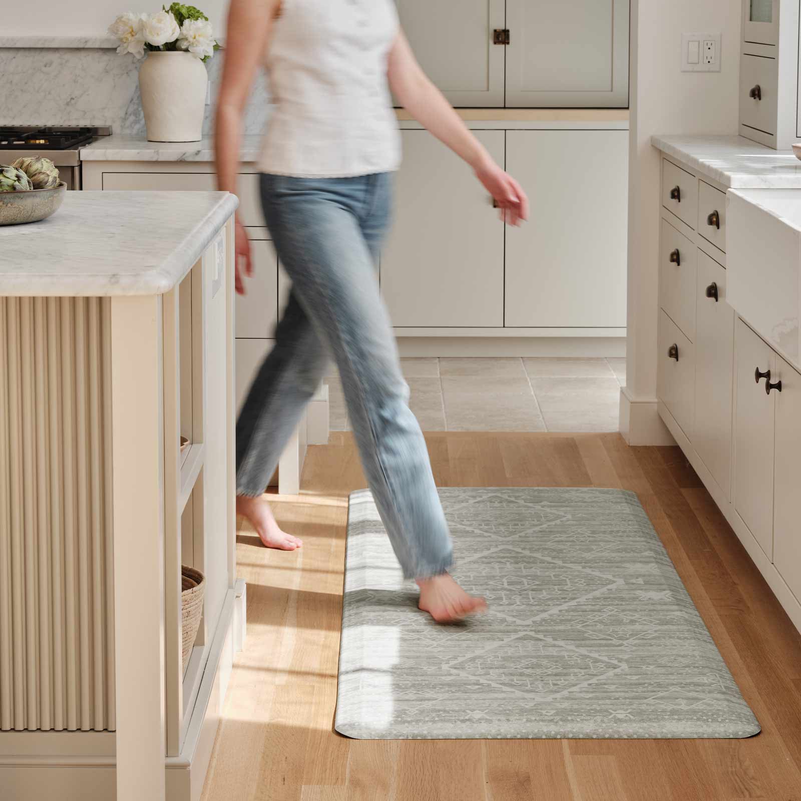 Ula Willow light green and white boho print standing mat shown in kitchen in size 30x72 with woman turning the corner around an island walking across the mat