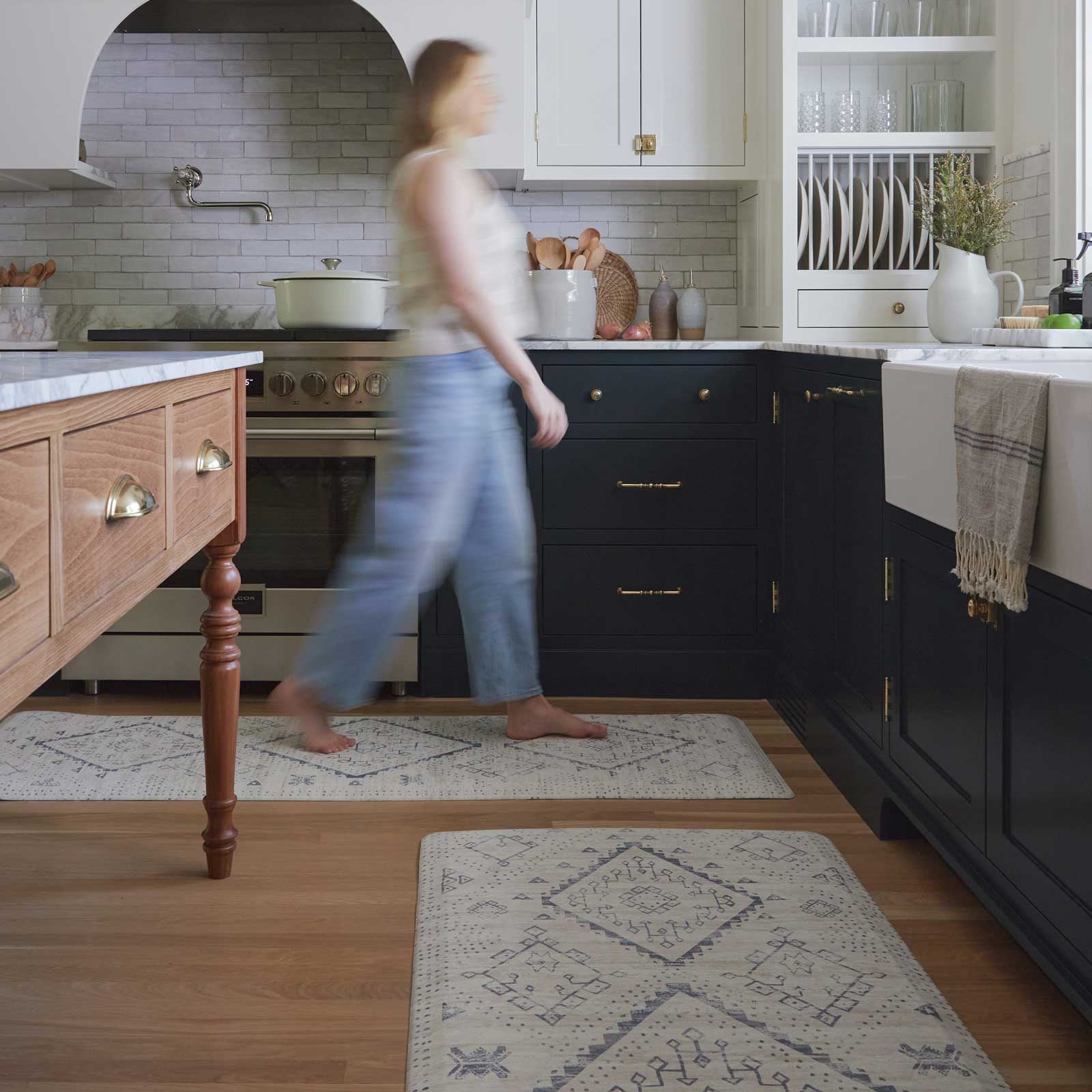 Ula Windmill blue and white boho print standing mat shown in a kitchen with size 30x72 and 22x72 in between the island and counter with woman walking across size 22x72 in the back