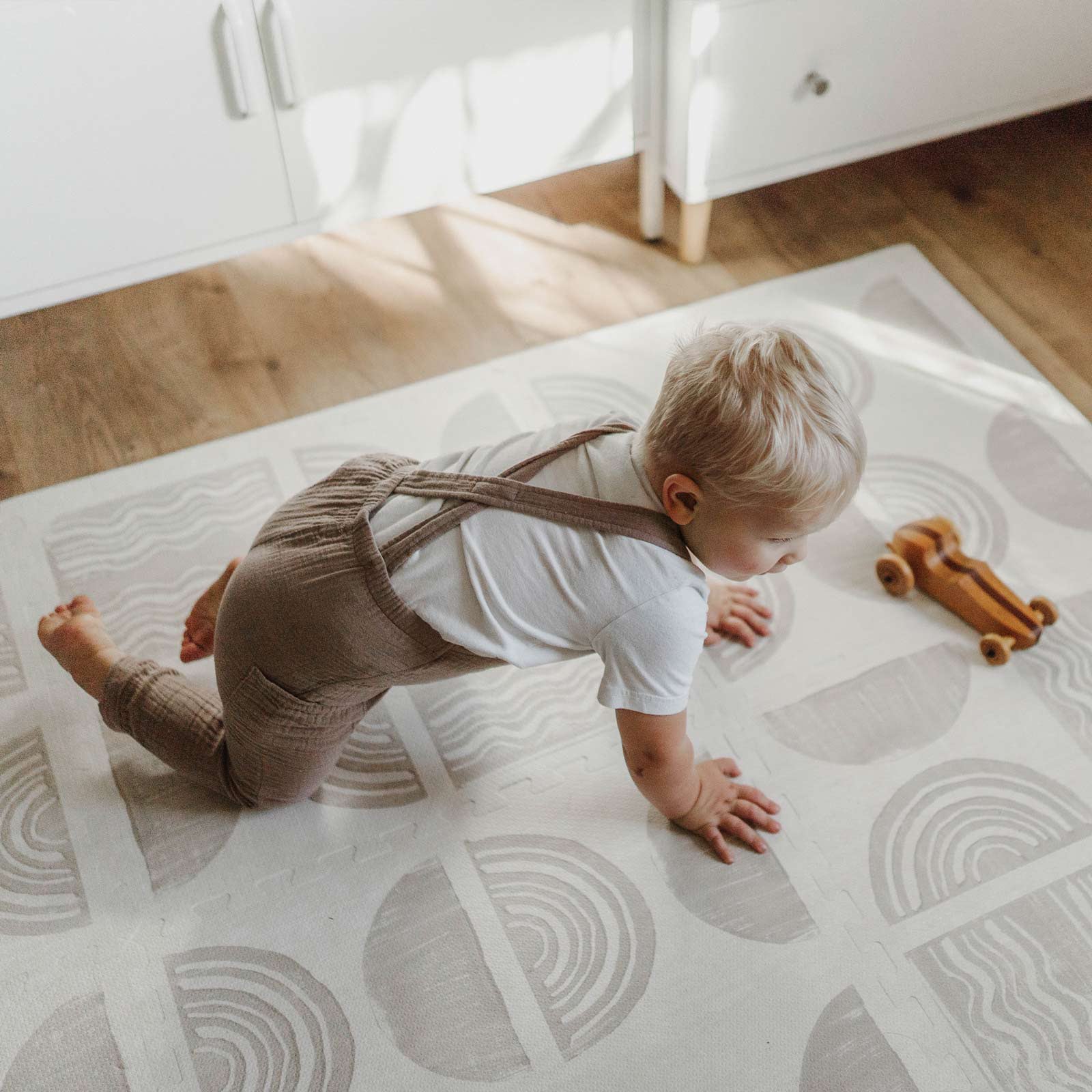 Ada pebble neutral block print play mat with toddler boy crawling on the mat playing with a wooden race car toy