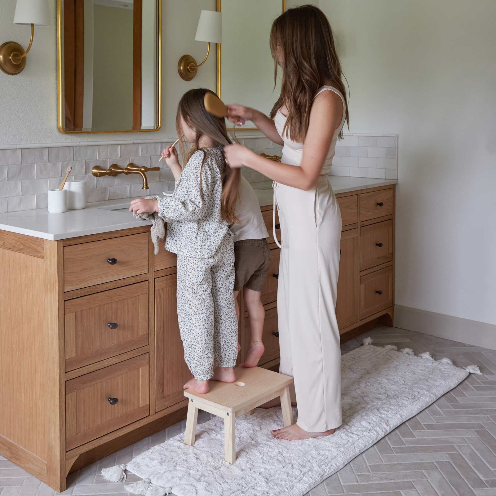 Arden wisp gray and white persian rug print bath rug shown in size 21x58 in front of a bathroom vanity with mom standing behind daughter on a stool while she does her hair