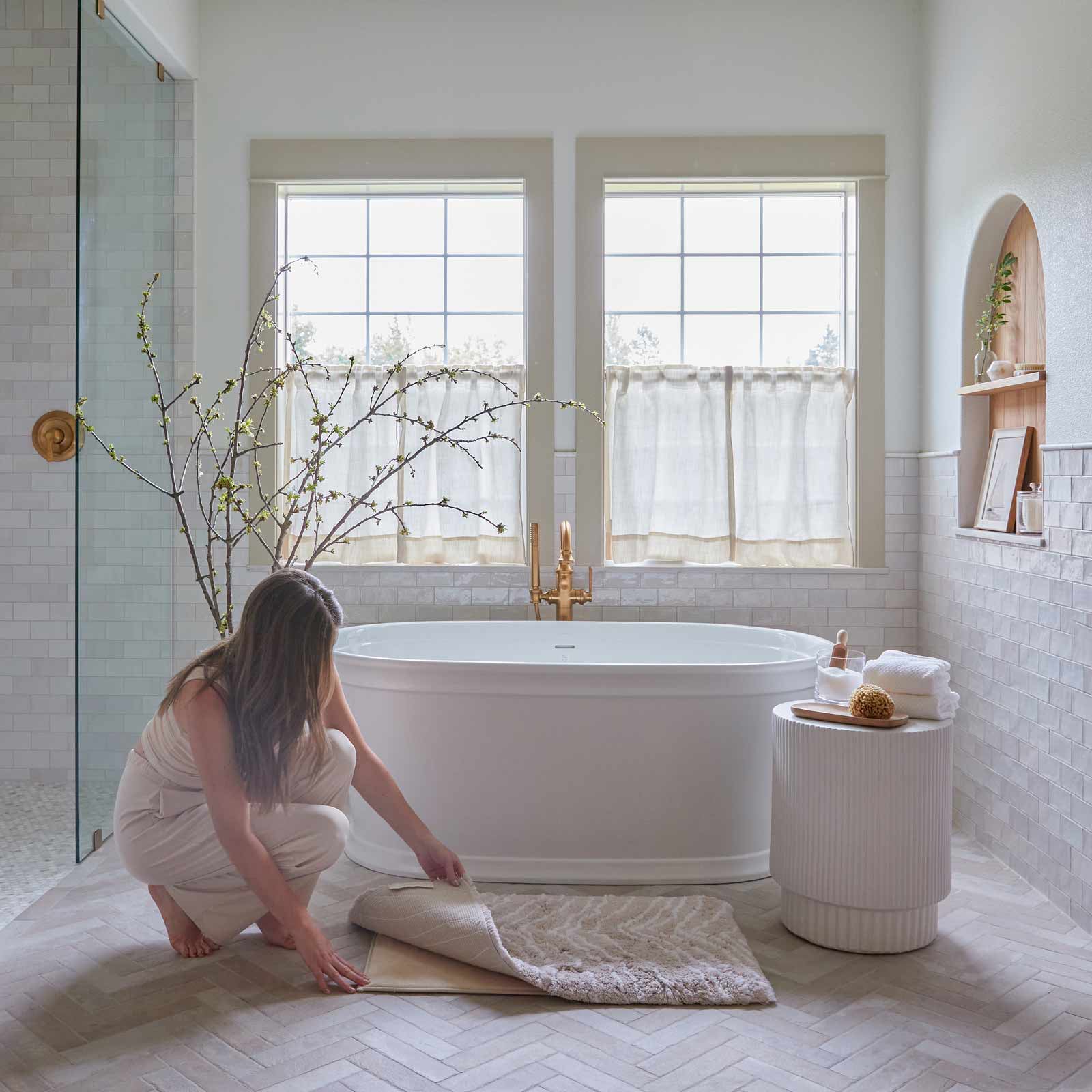 Zelda shell neutral zebra print bath rug shown in size 21x34 in front of a bath tub with woman kneeling on the ground to lift up the corner of the mat to show the liner beneath