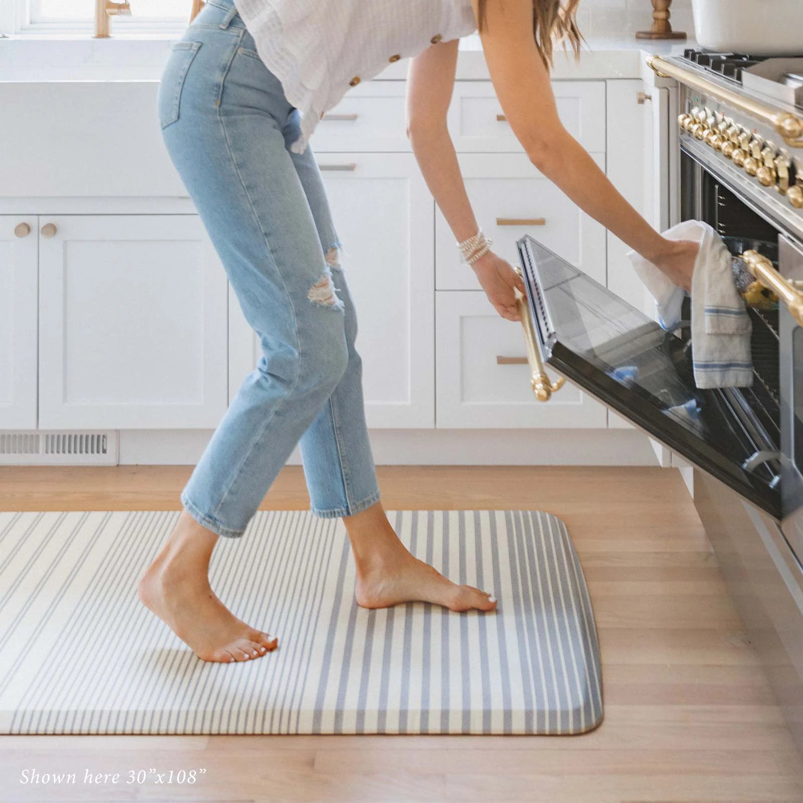 Blue and white minimal stripe kitchen mat in size 30x108 in kitchen with woman taking food out of the oven.