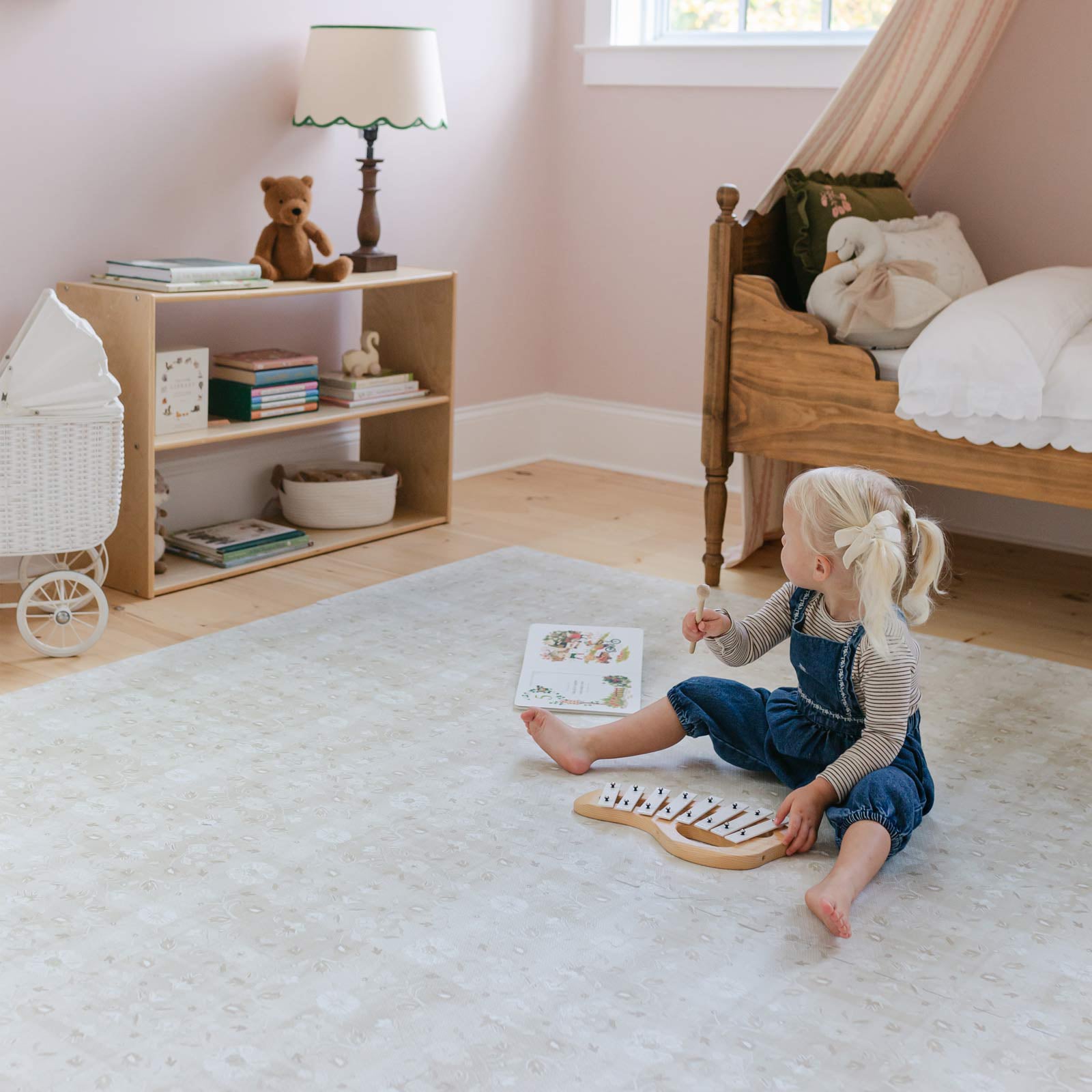 Gemma Chateau neutral floral play mat shown in a pink bedroom with toddler girl sitting on the mat playing with a xylophone and book