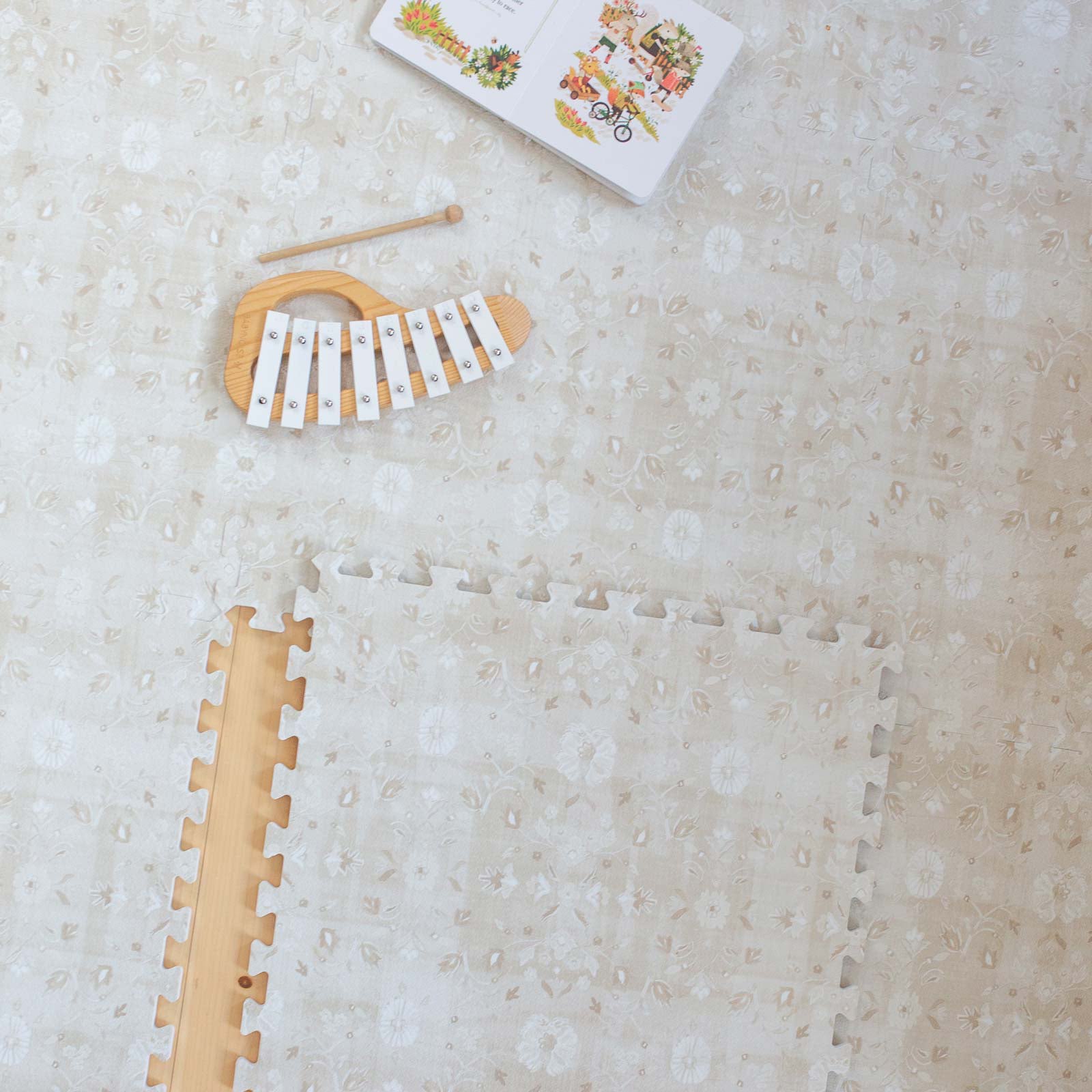 Gemma Chateau neutral floral play mat shown from above with 1 tile exposed and xylophone and book on the mat