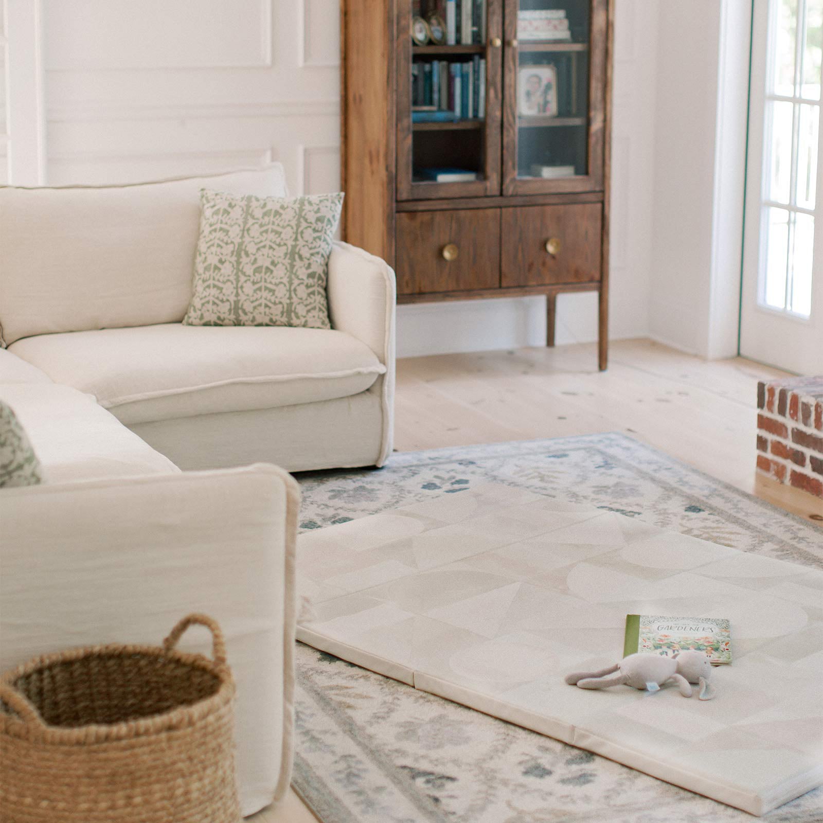 Boden stonewash neutral geometric print foldable play mat shown laid out on the floor of a living room with stuffed bunny and storybook on the mat