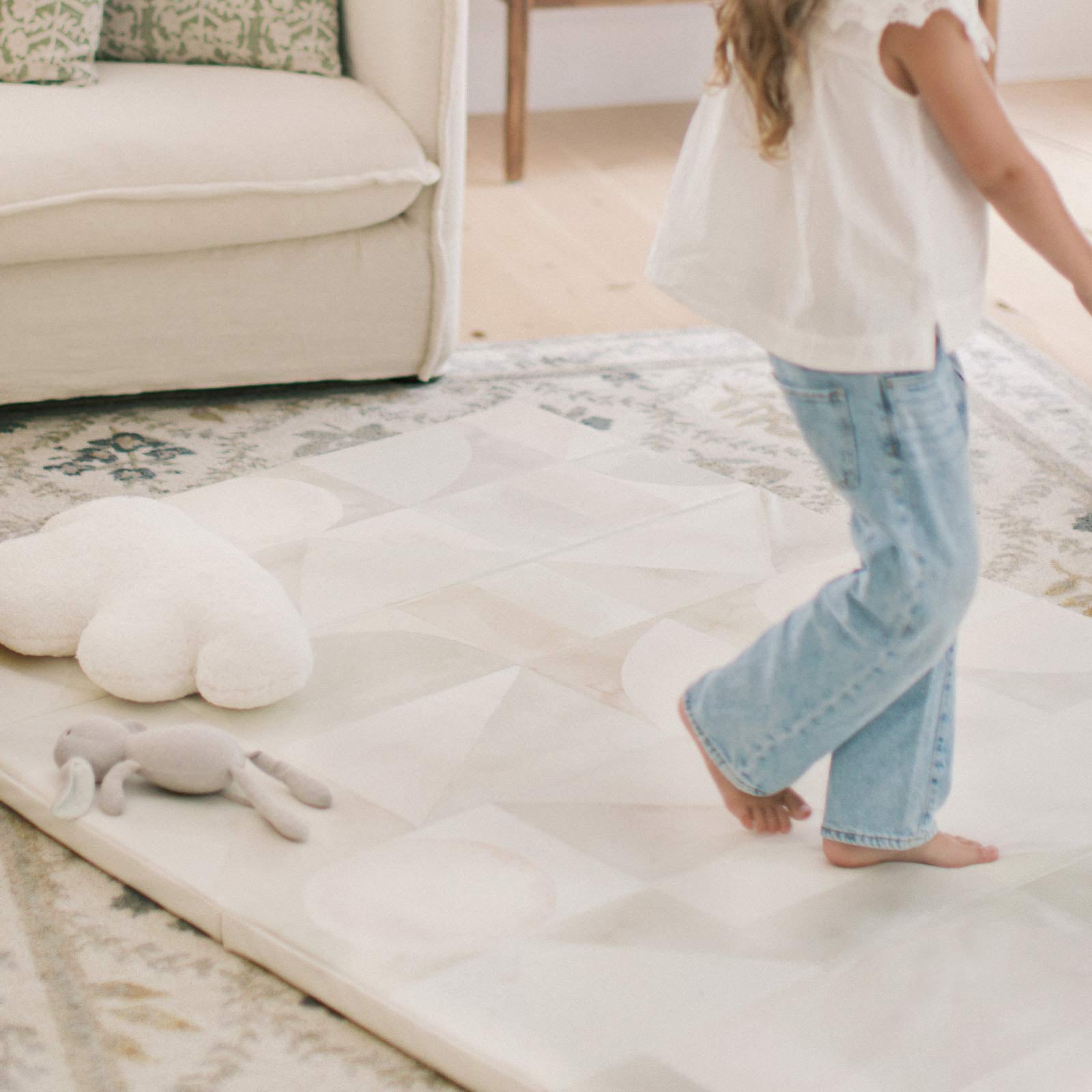 Boden stonewash neutral watercolor geometric print foldable play mat shown in living room with little girl walking across the mat