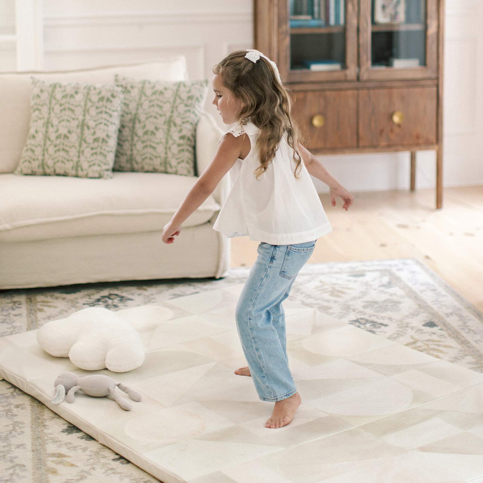 Boden stonewash neutral watercolor geometric tumbling mat on top of a rug  in a living with a little girl twirling on the mat 