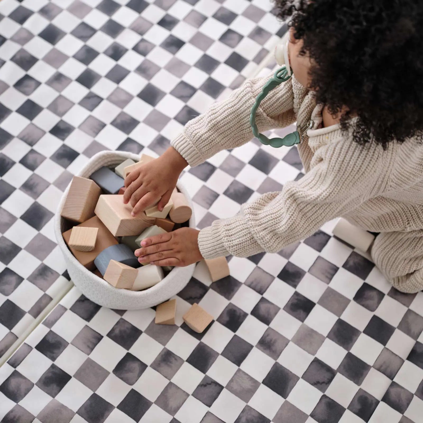 Tuxedo black and white checker print tumbling mat with toddler reaching into a basket of wooden blocks