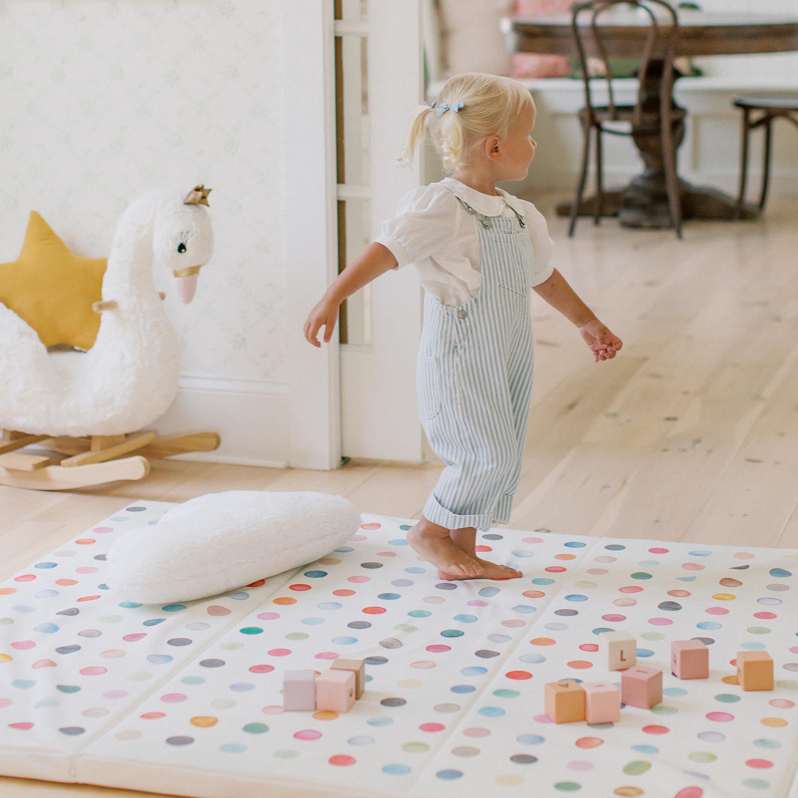 Dottie gloria multi color polkadot print tumbling mat shown in a play room with wooden blocks and pillow on top and little girl jumping around on the mat