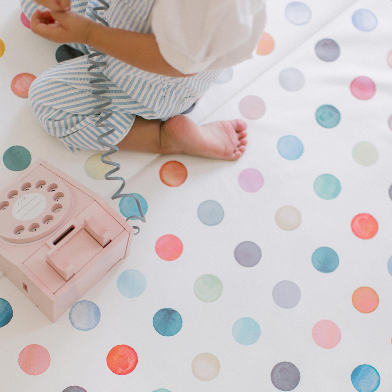 Dottie gloria multi color polkadot print tumbling mat shown with little kneeling on the mat playing with a toy phone