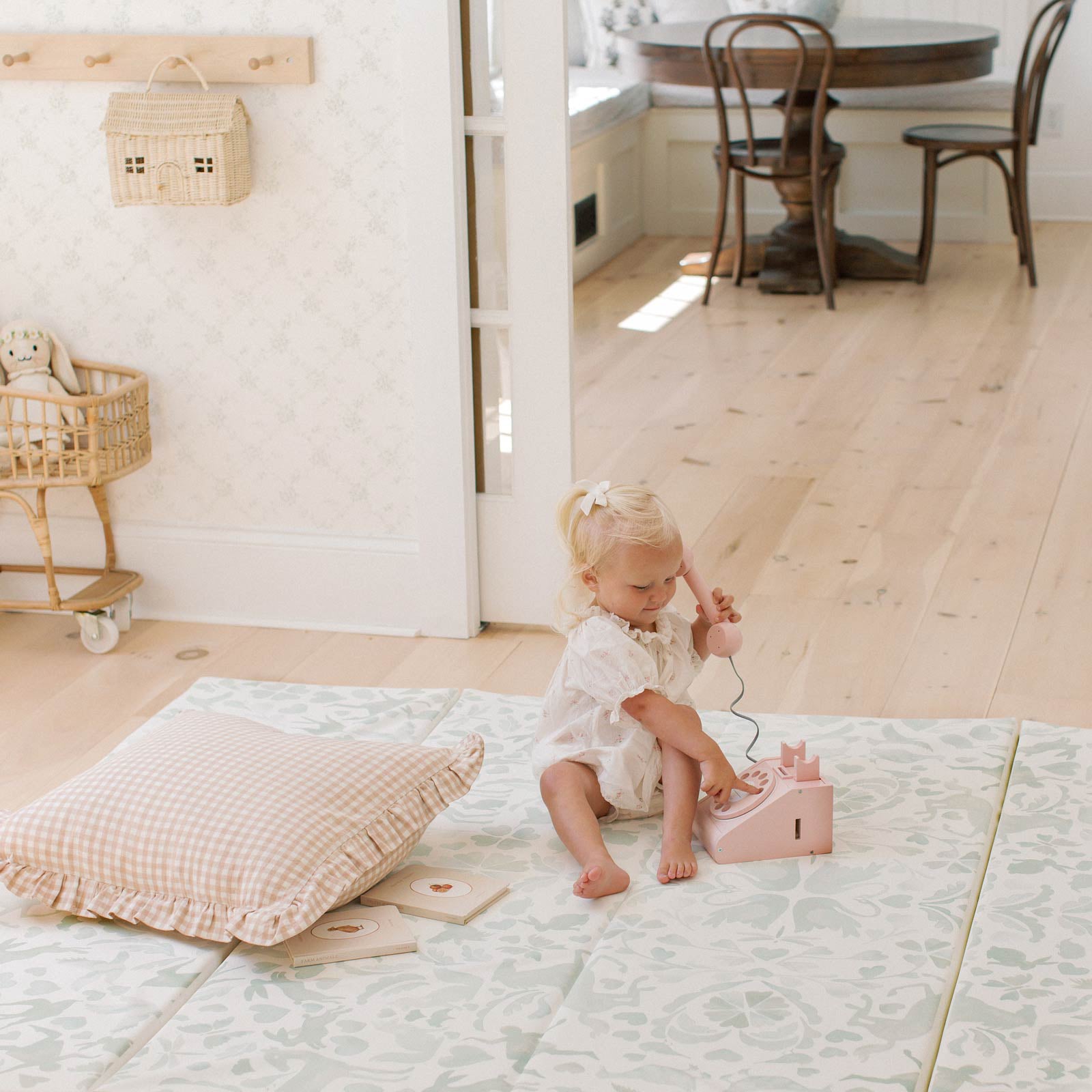 Folklore mint green storybook pattern tumbling mat in a living room with toddler girl sitting on the mat next to a pillow dialing a play telephone