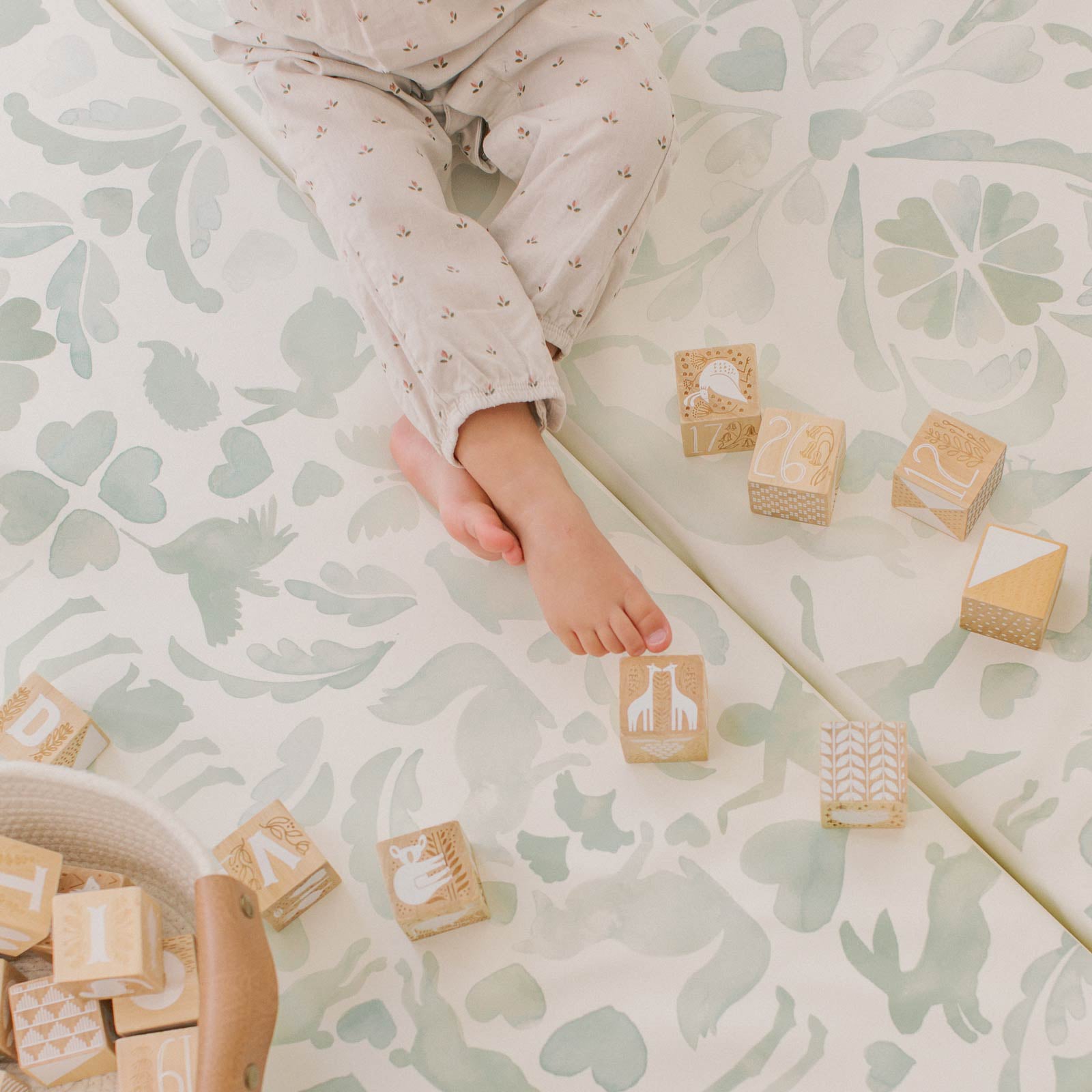 Folklore mint green storybook pattern tumbling mat shown with toddlers foot and wooden blocks laid out on the mat