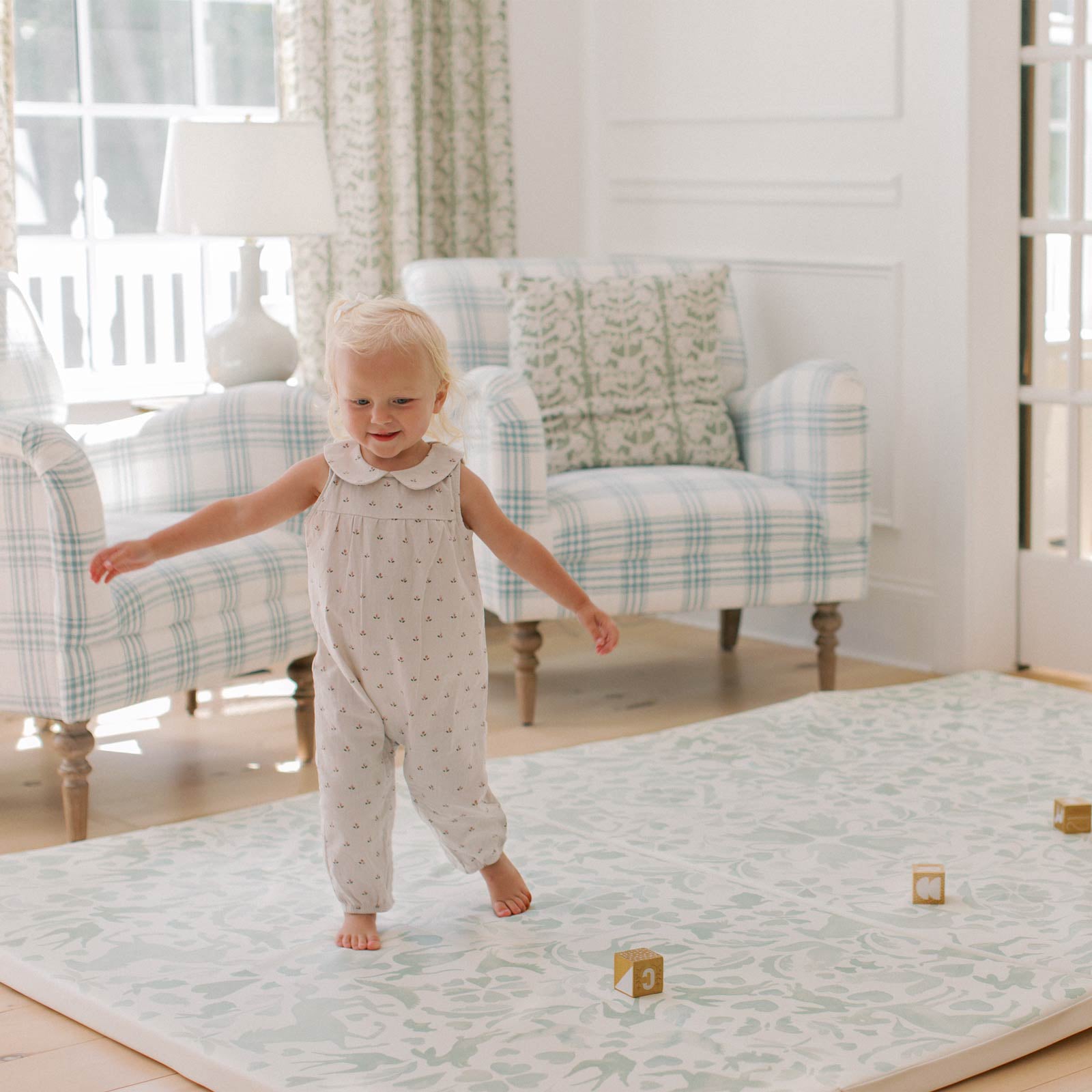 Folklore glass mint green storybook pattern tumbling mat shown in living room with toddler girl in motion and wooden blocks on the mat 