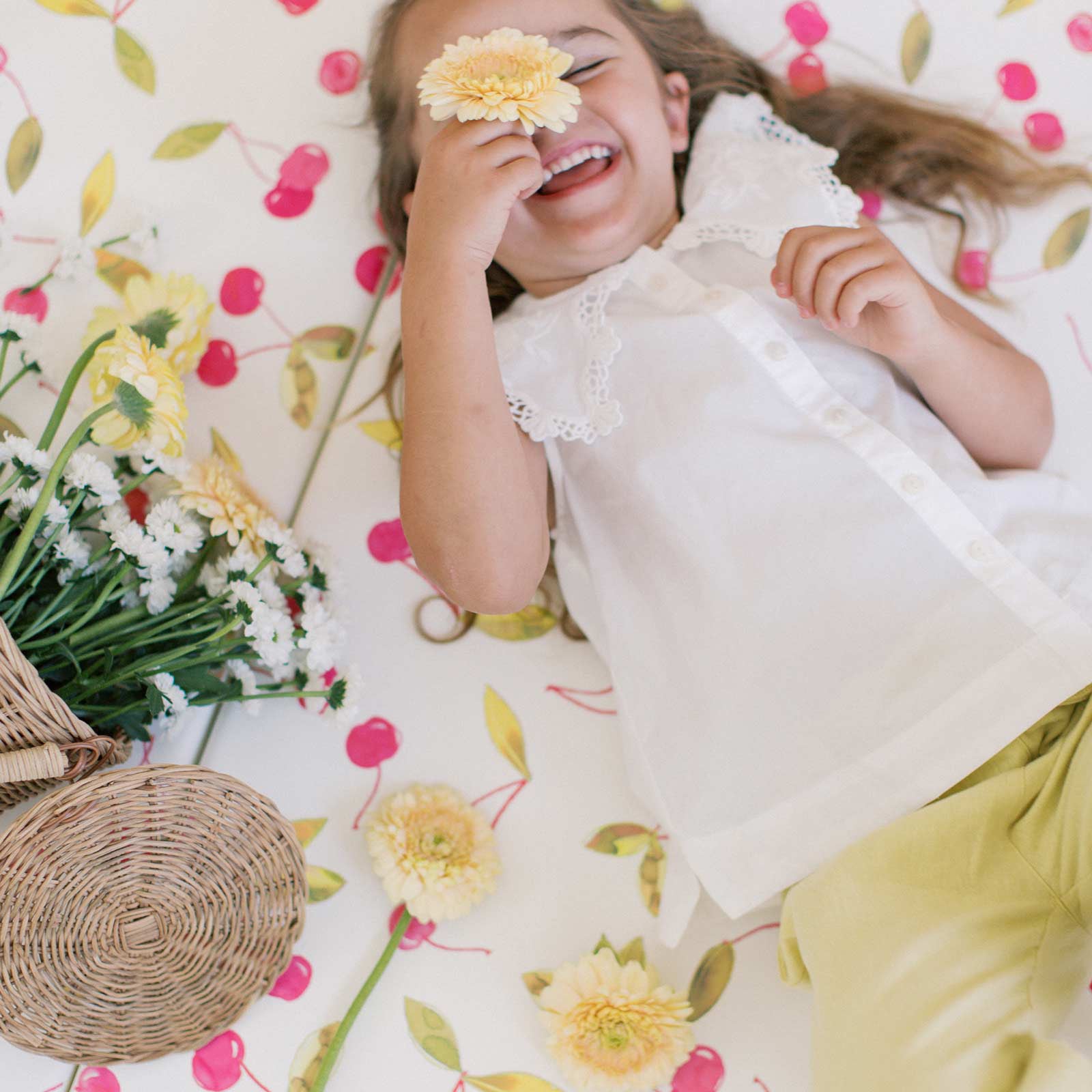 Lulu red and green Cherry print tumbling with little girl laying on the mat laughing holding daisies