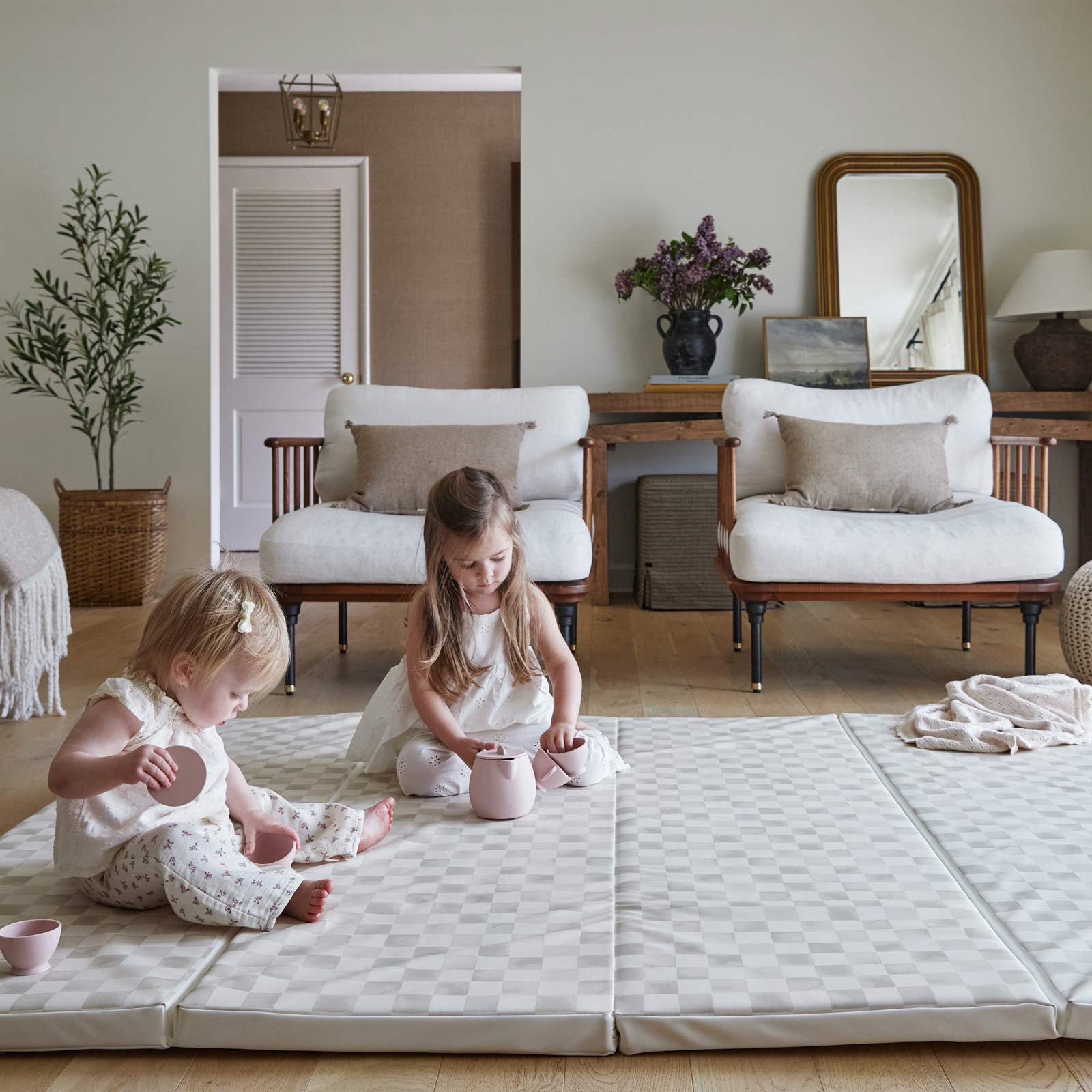 Almond neutral checker print tumbling mat shown in living room with 2 little girls playing with a tea set on the mat