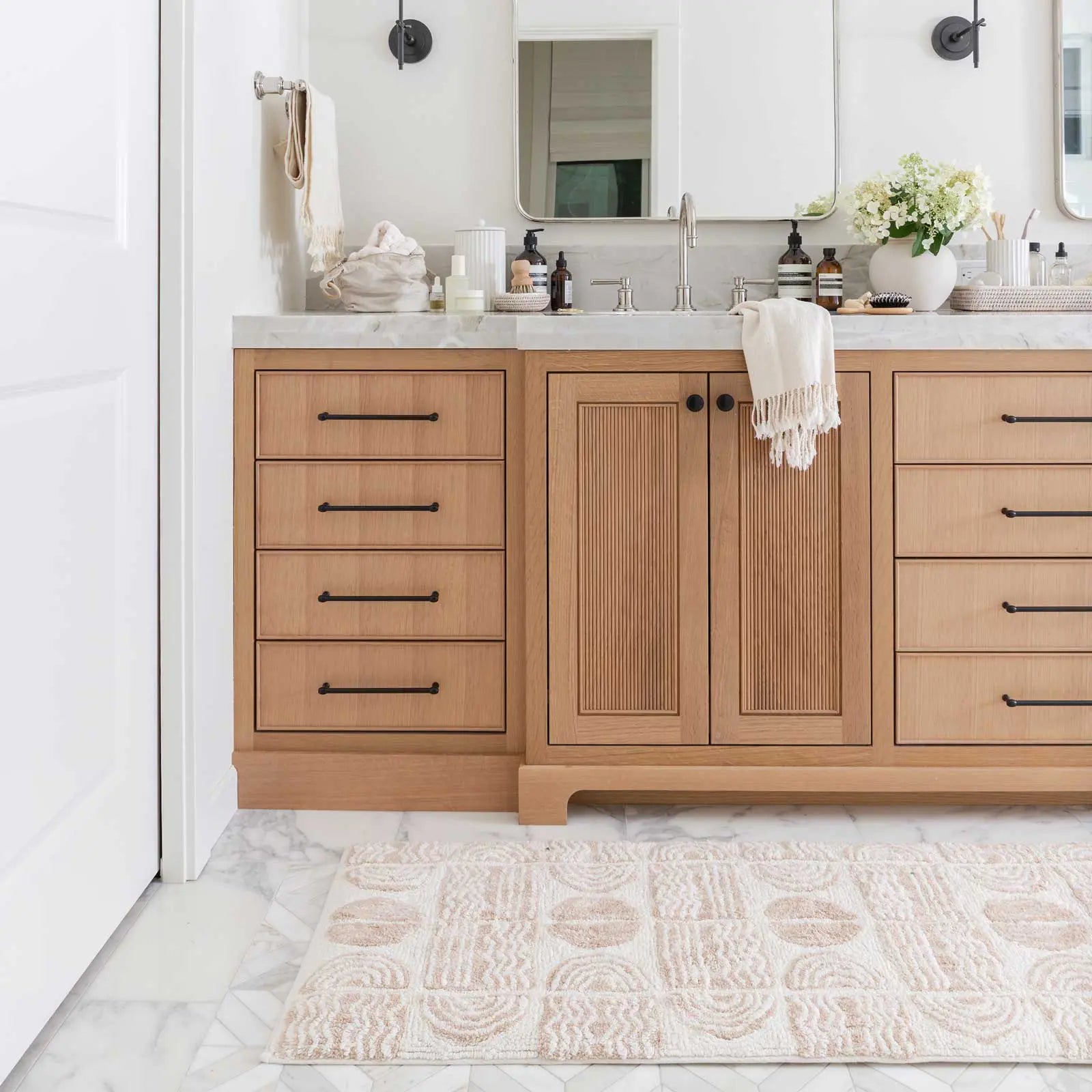 Ada Pebble neutral and white geometric print bath mat shown in size 21x58 in front of a bathroom double vanity