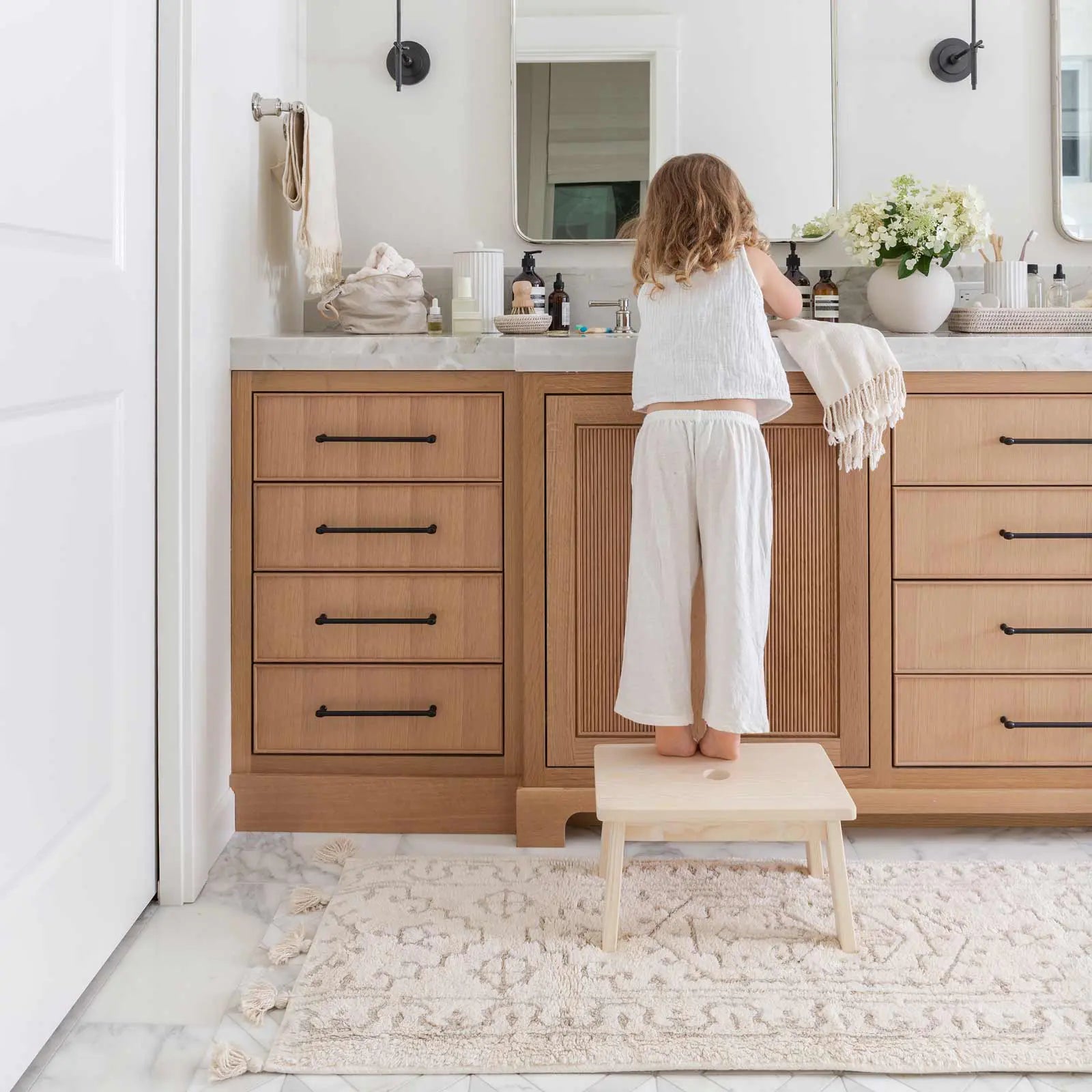 Arden pearl cream and white persian rug pattern bath mat in size 21x58 in bathroom in front of vanity with little girl standing at the sink on a stool