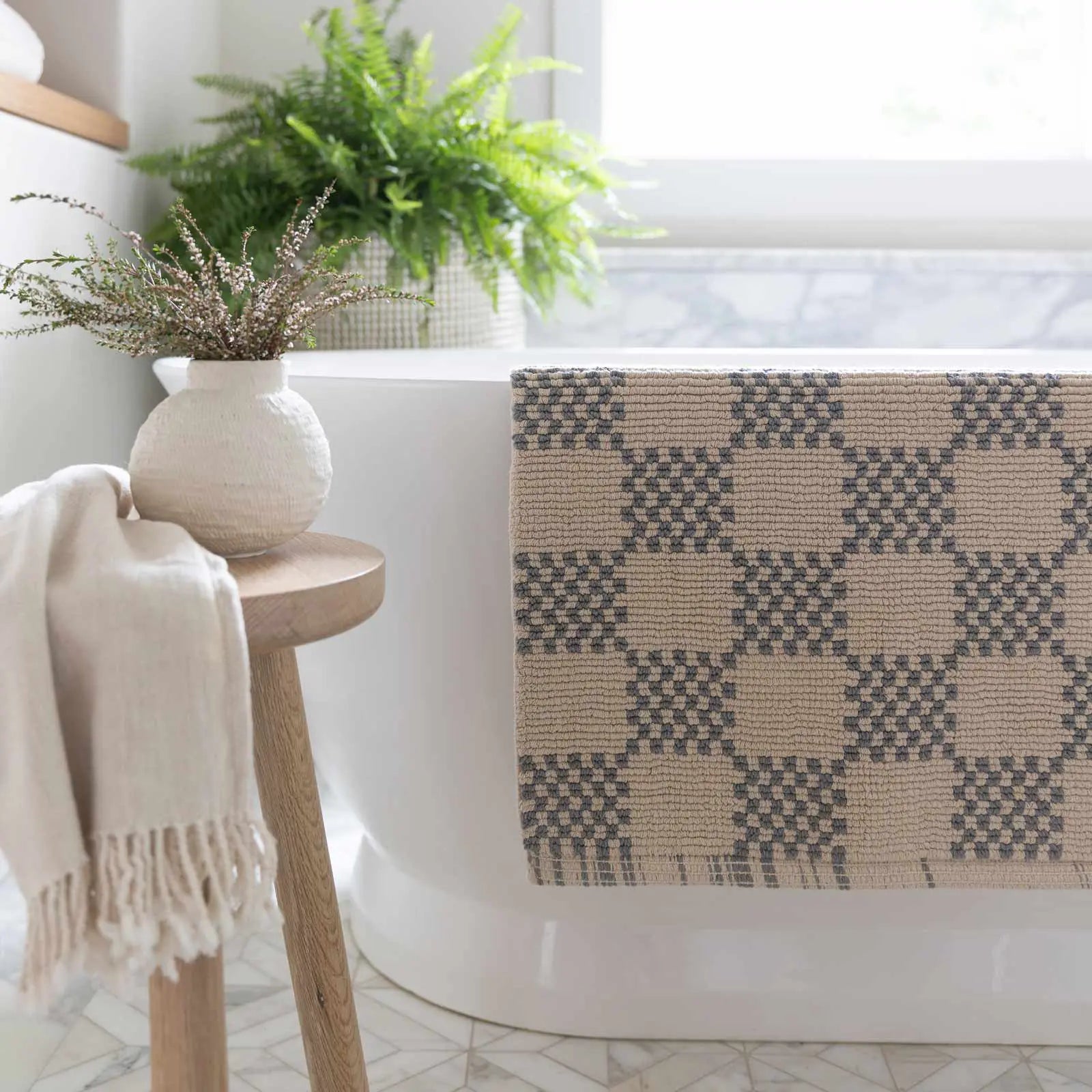 Bath mat in checker harbor gray print in size 21x34 hanging over the edge of a bath tub