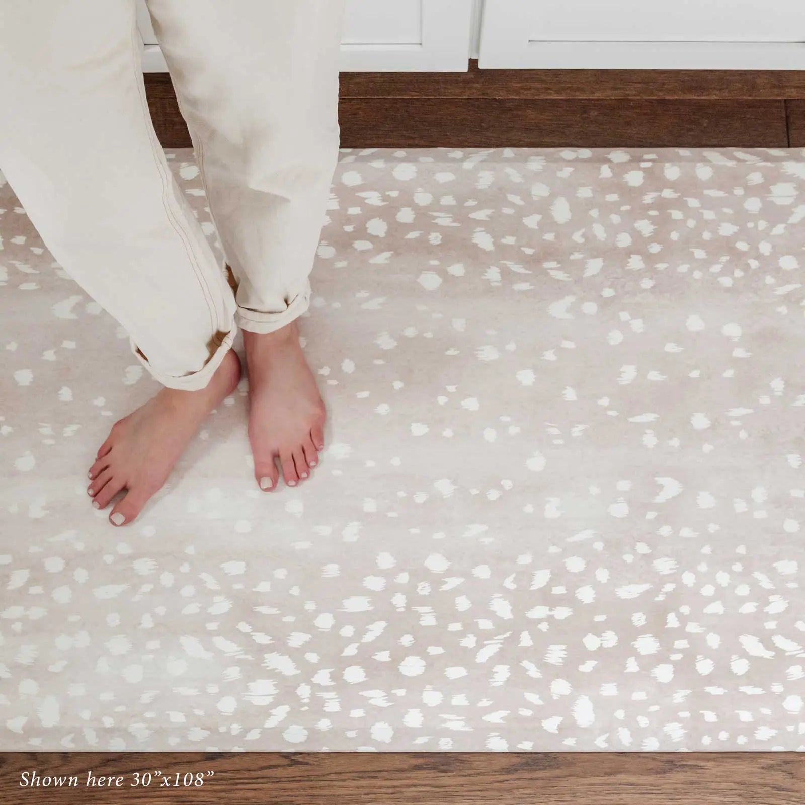 Fawn brown neutral animal print kitchen mat shown with woman's feet standing on size 30x108