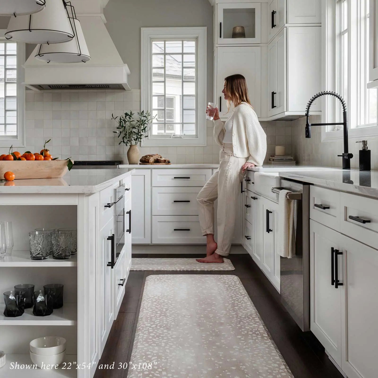 Fawn brown neutral animal print kitchen mat shown in kitchen in sizes 22x54 and 30x108 with woman standing on size 22x54 drinking a glass of water