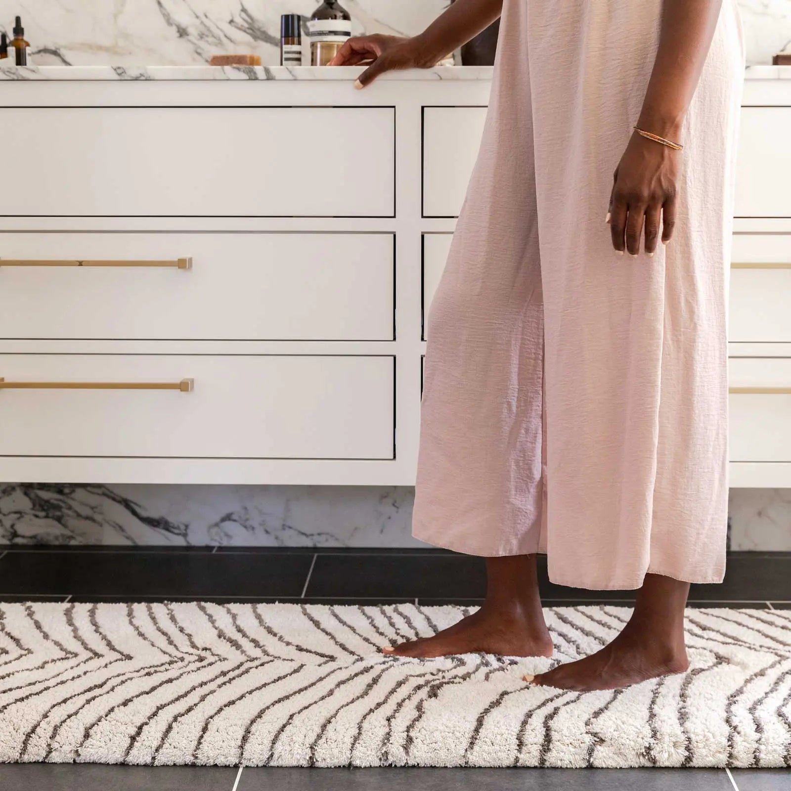 Zelda puffin cream and gray zebra print bath mat in size 21x58 in front of a bathroom vanity with woman standing on the mat