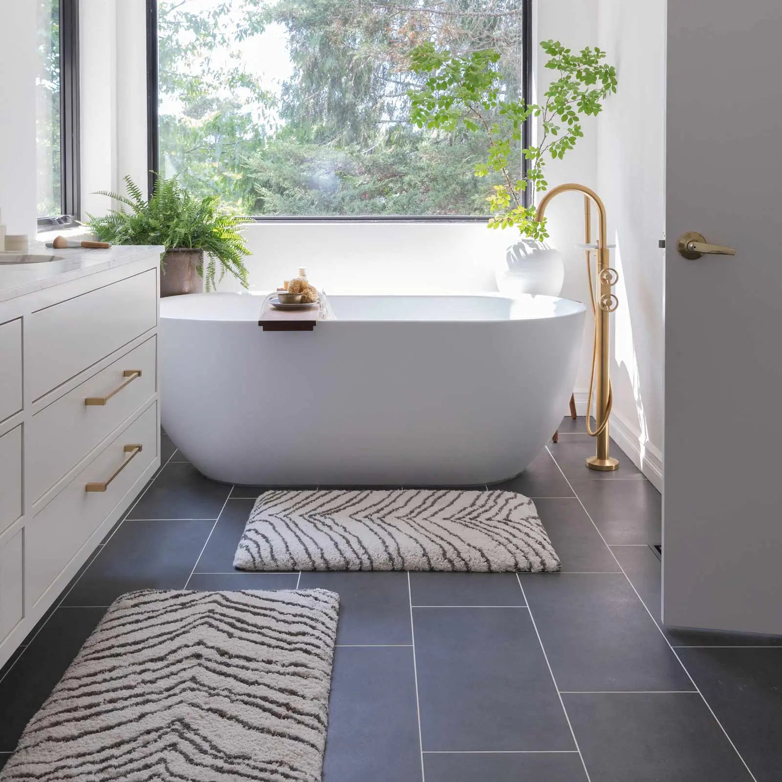 Zelda puffin cream and gray zebra print bath mat shown in a bathroom with size 21x58 in front of a double vanity sink and size 21x34 in front of a bath tub