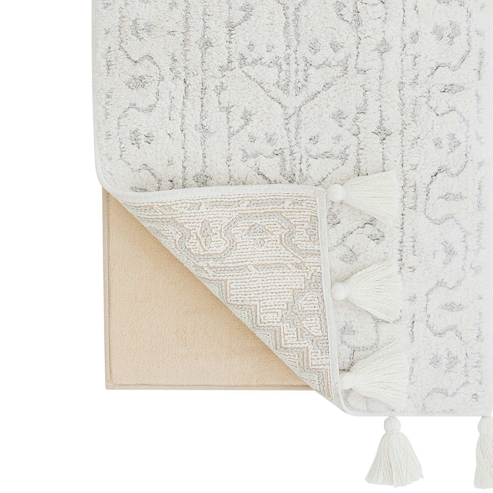 Corner of the Arden wisp gray and white persian rug print bath mat lifted up to show the foam pad beneath