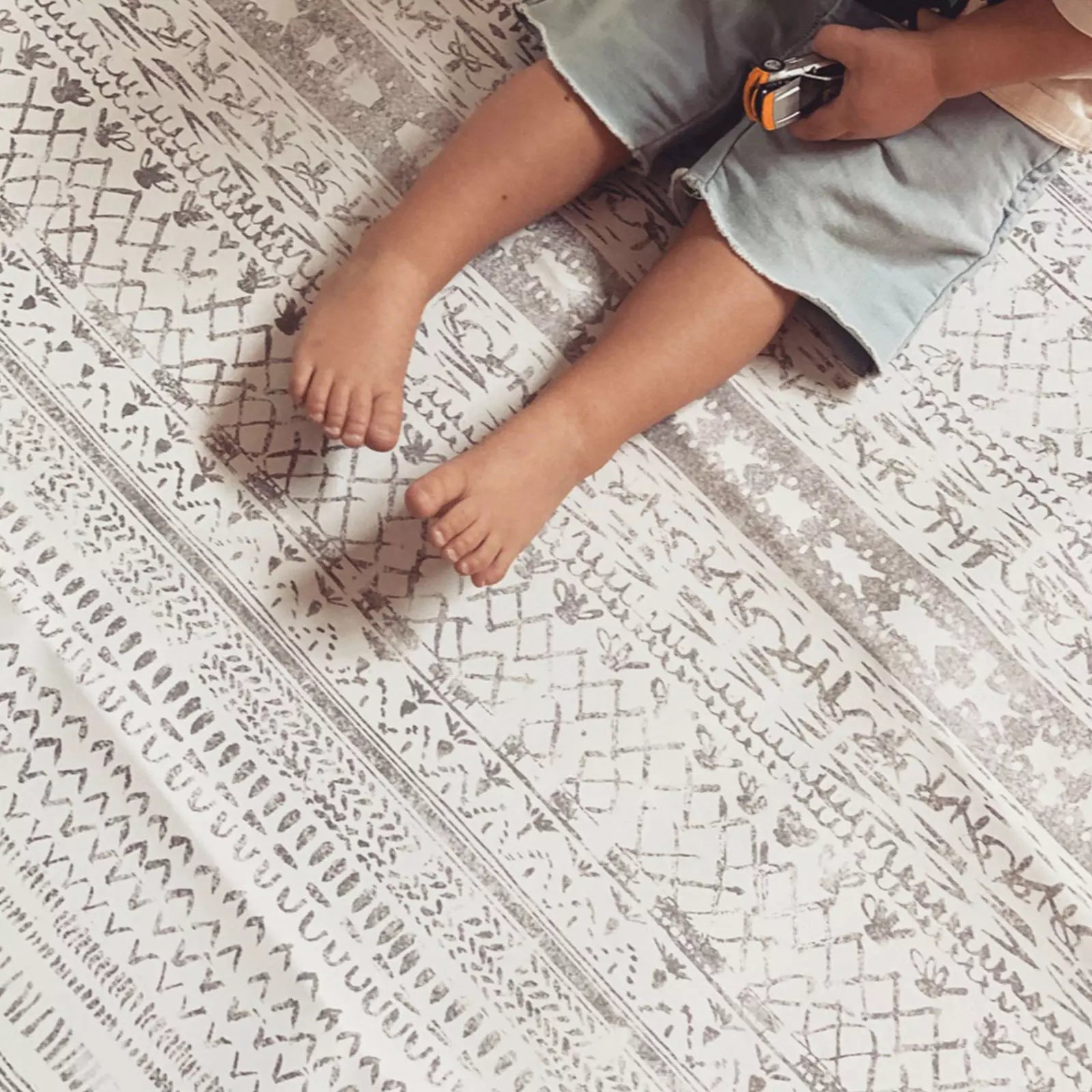 Skipping Stone gray and white striped highchair mat shown up close with baby feet